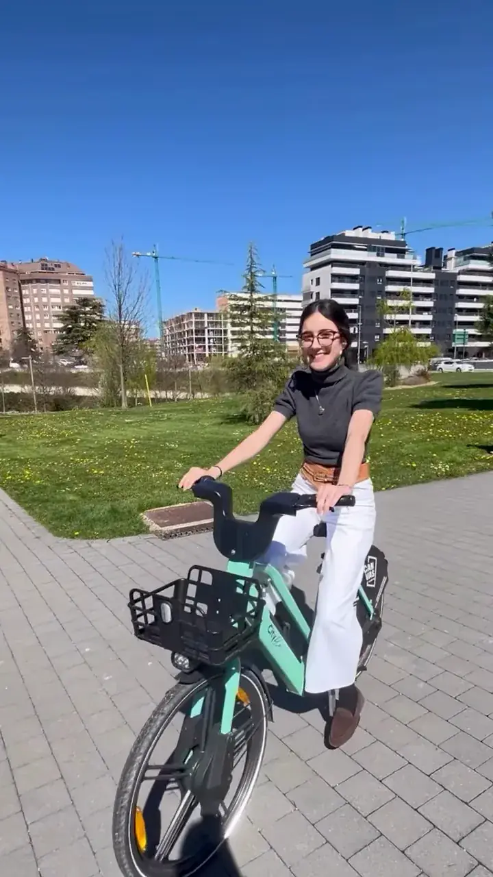Estudiante sonriente en una bici eléctrica Cityflow verde, por un paseo junto a un parque