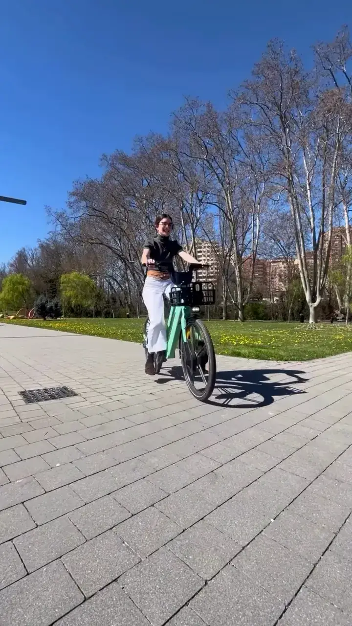 Estudiante en una bici eléctrica Cityflow verde por un paseo con árboles